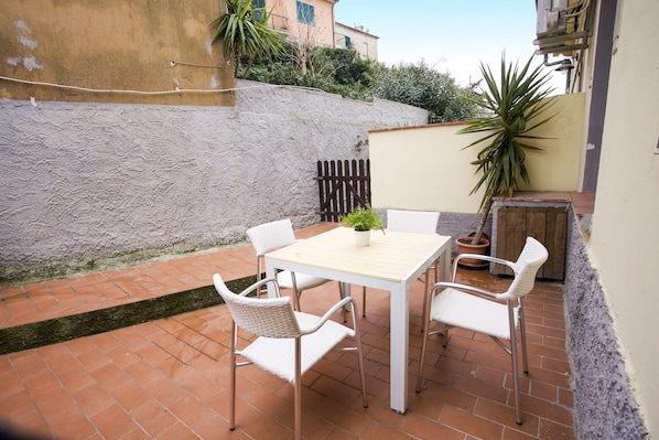 An outdoor patio with a white table and chairs, surrounded by a brick floor and a low stone wall.