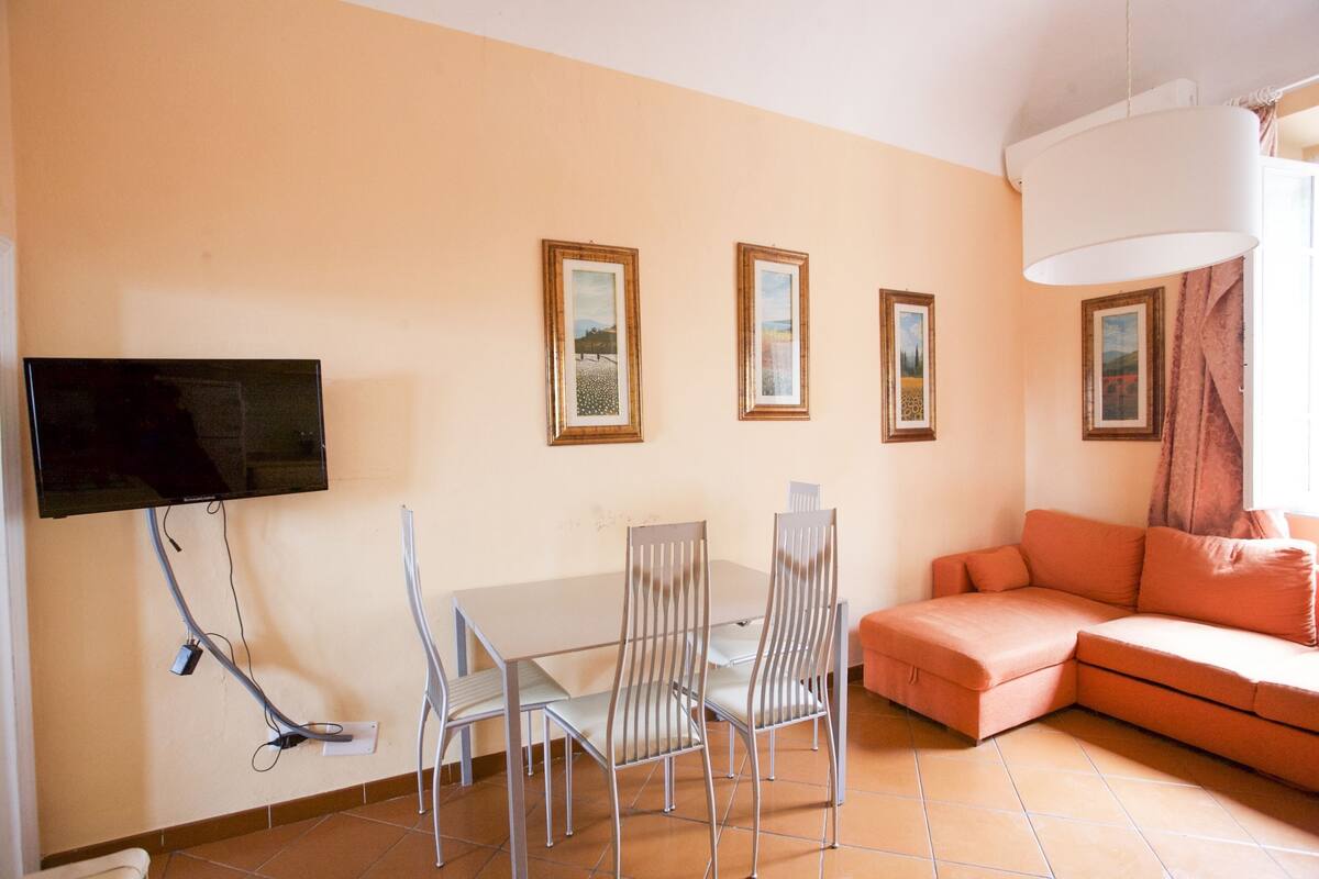 A living room with a TV mounted on the wall, a dining table with chairs, and a sofa.