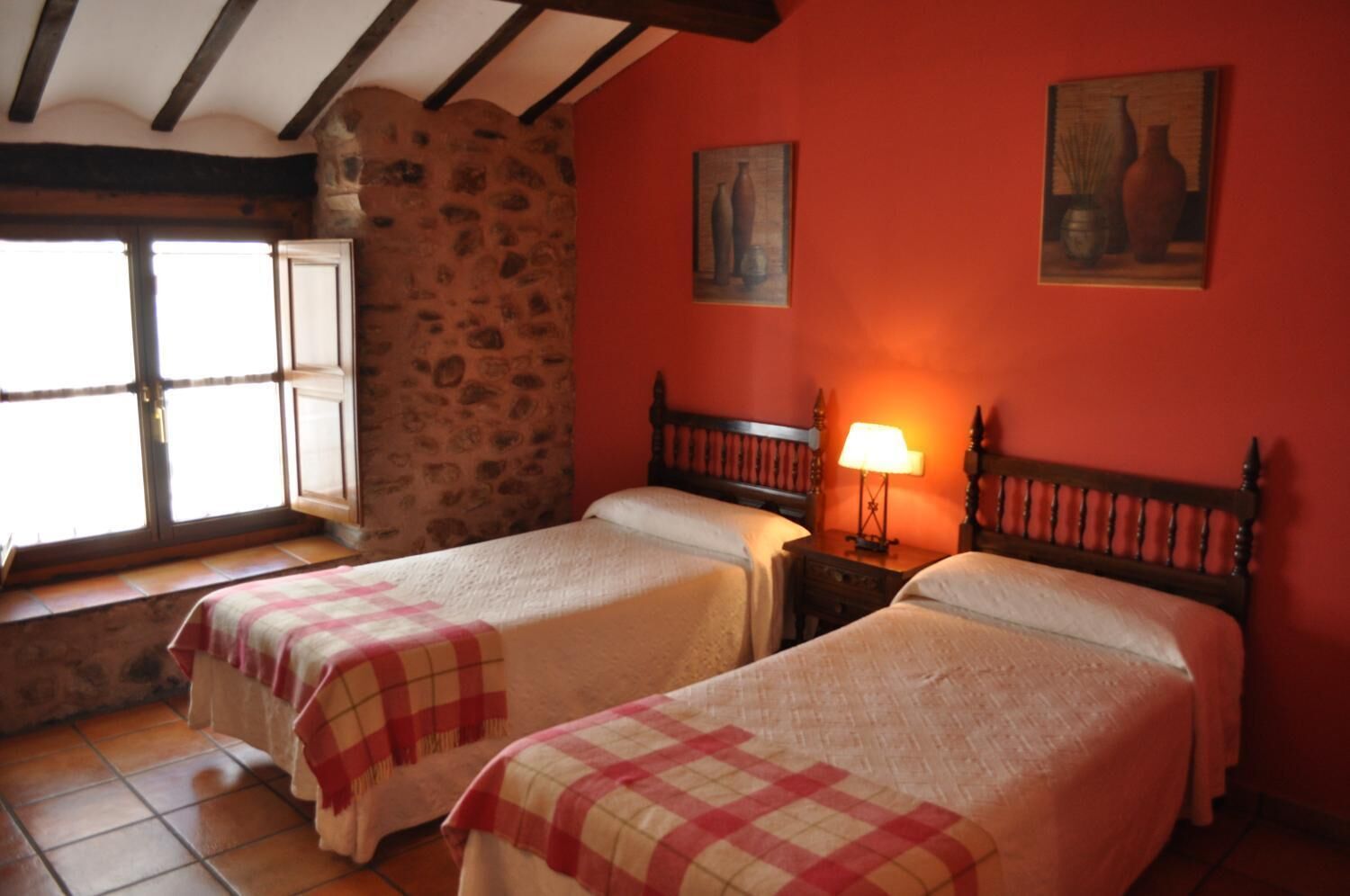 A room with two beds, a stone wall, a window with a view, and two paintings on the wall.