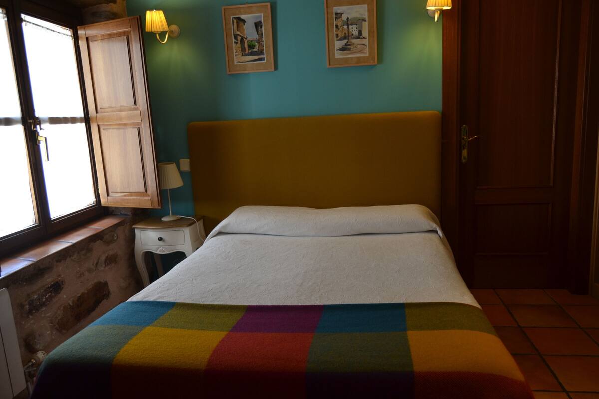 A bedroom with a bed, a window, a nightstand, and two wall-mounted lamps.