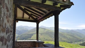 Una estructura rústica de piedra con techo de madera y vista a ondulantes colinas y montañas al fondo.