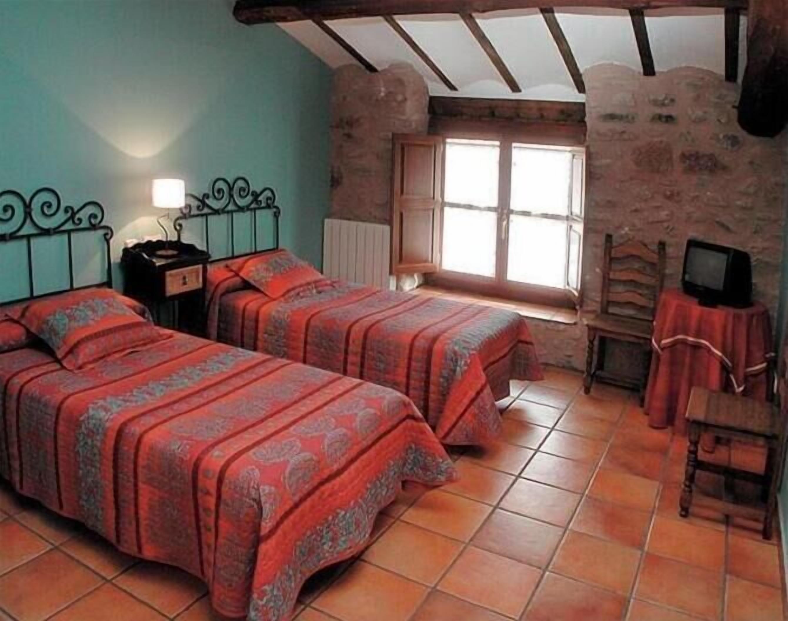 Een kamer met twee bedden, een raam, een radiator en een televisie op een tafel.