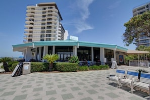 A beachfront hotel with a curved roof, outdoor seating, and a palm tree.