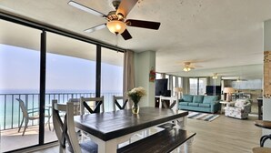 Un salon spacieux comprenant une grande table à manger, un canapé et un téléviseur. Un balcon offre une vue sur l’océan.