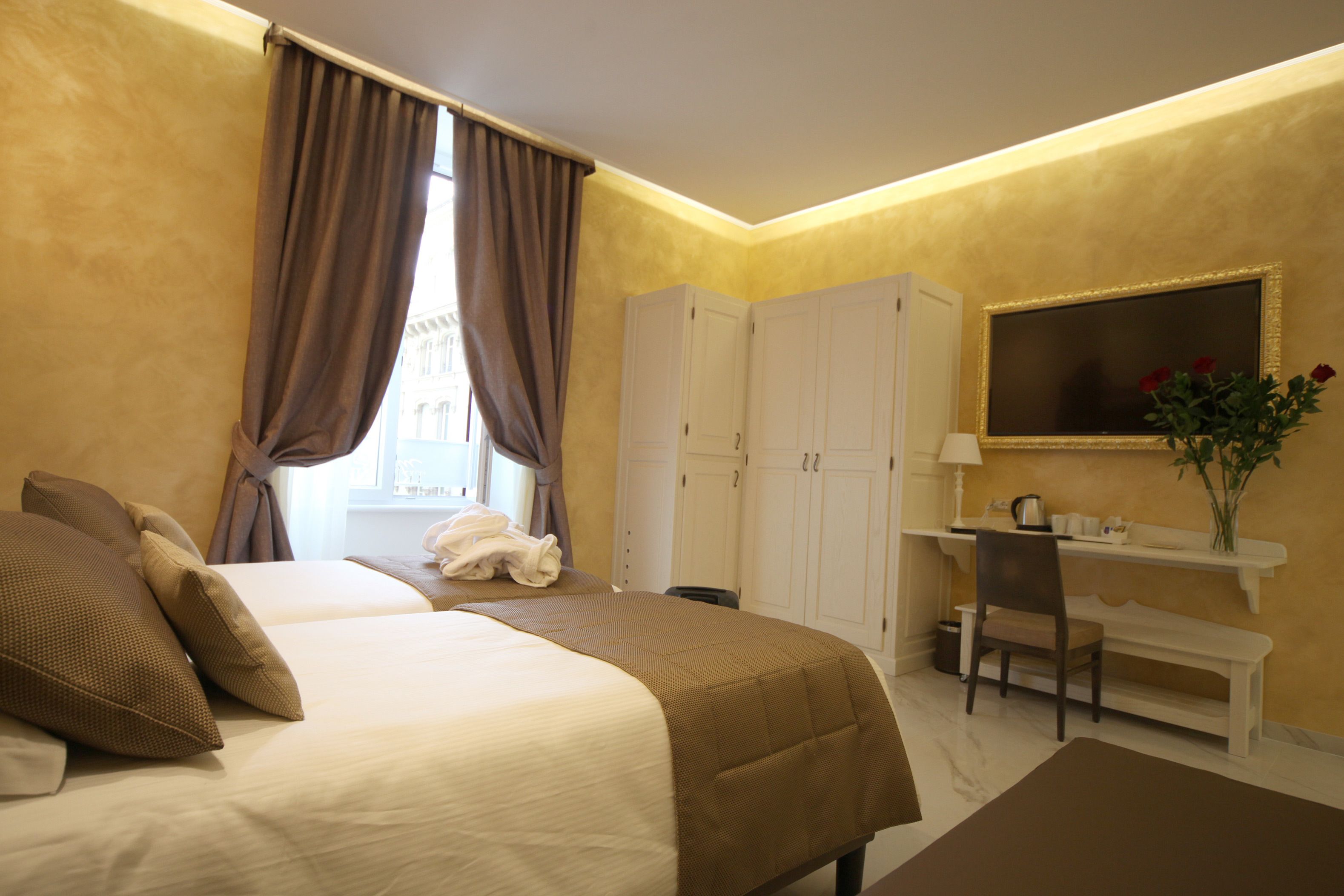 A hotel room with a bed, a desk, a chair, a mirror, and a window with curtains.