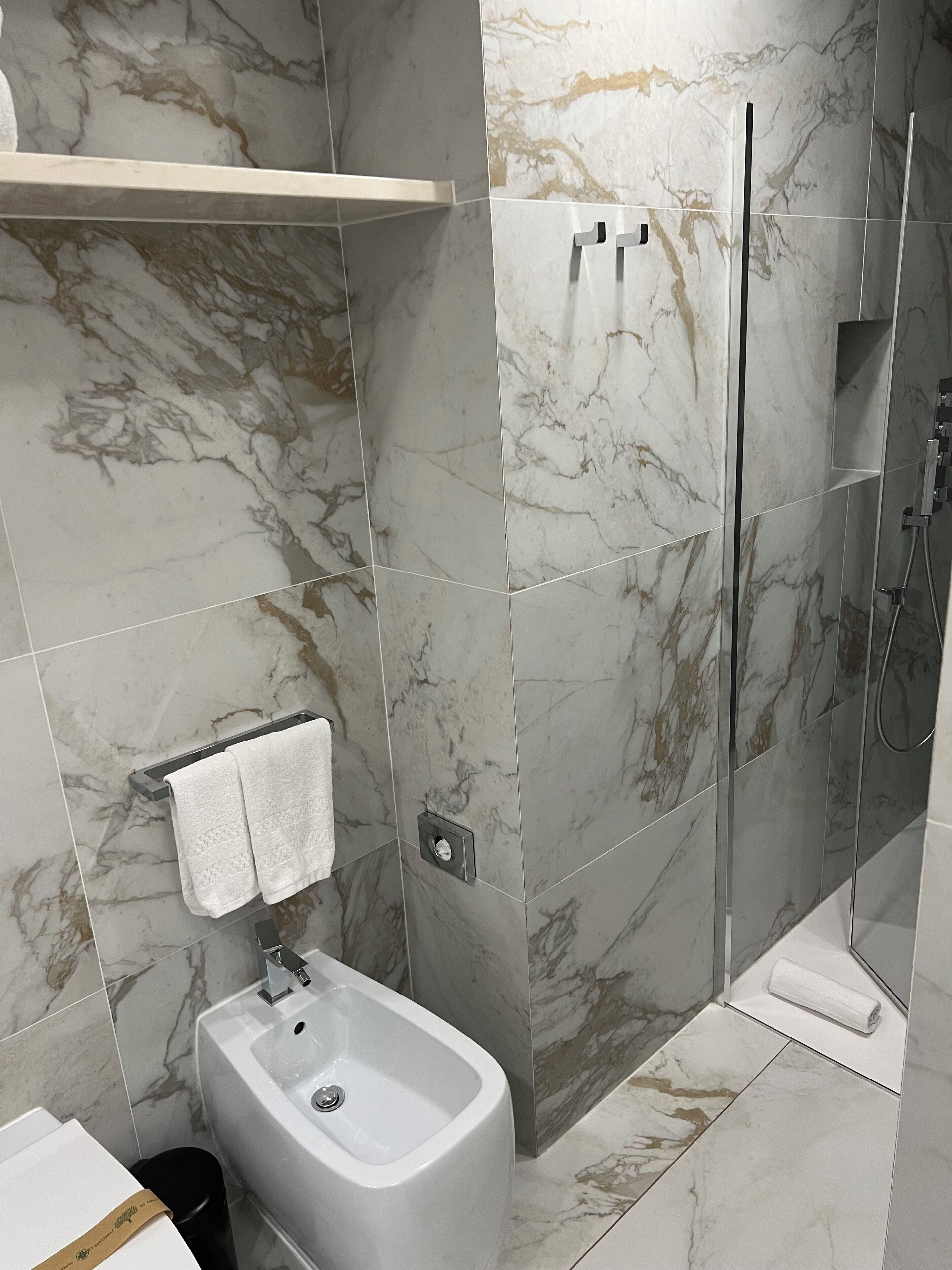 A bathroom with a bidet, a shower, and marble tiles.