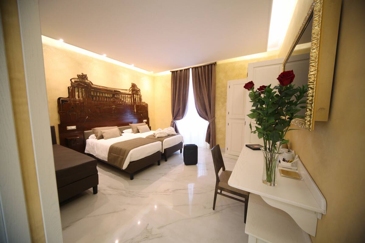 Habitación de hotel con una cama grande, un escritorio con silla, un espejo y un florero con flores.