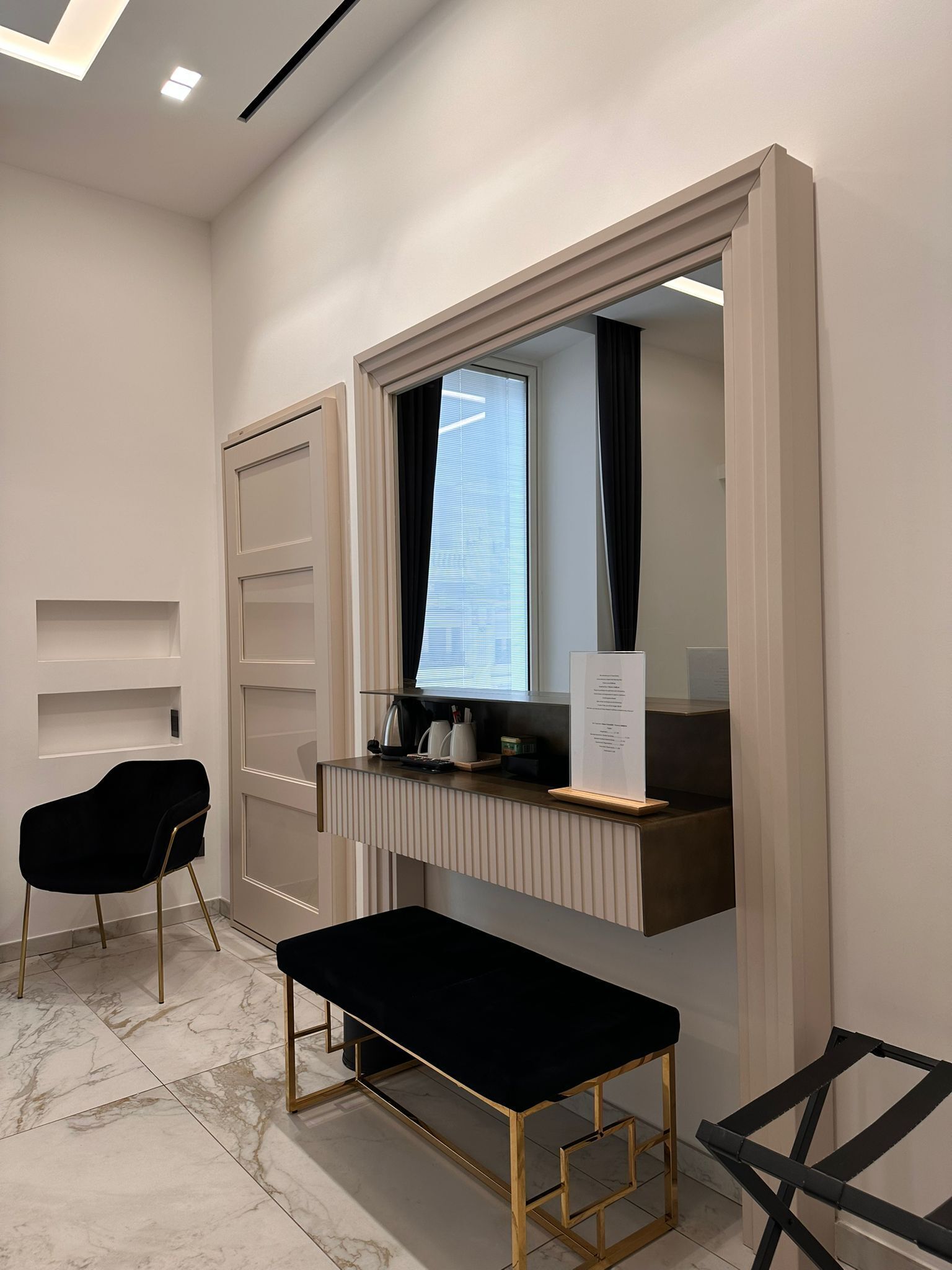A modern room with a black bench, a desk with a computer, and a window with blinds.
