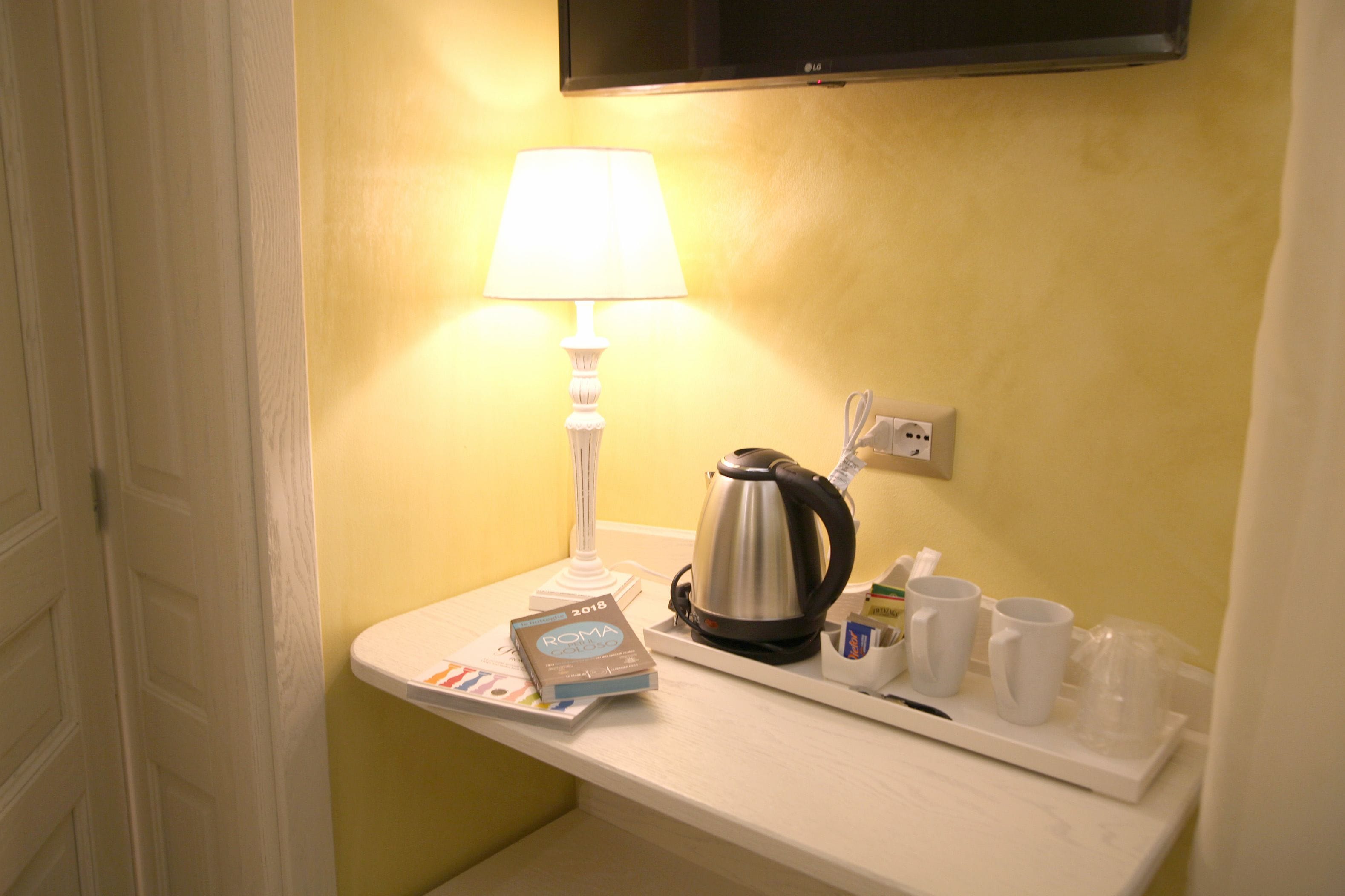 Une salle de bain d’hôtel avec un comptoir blanc, une lampe, une bouilloire et un plateau contenant des tasses et un livre.