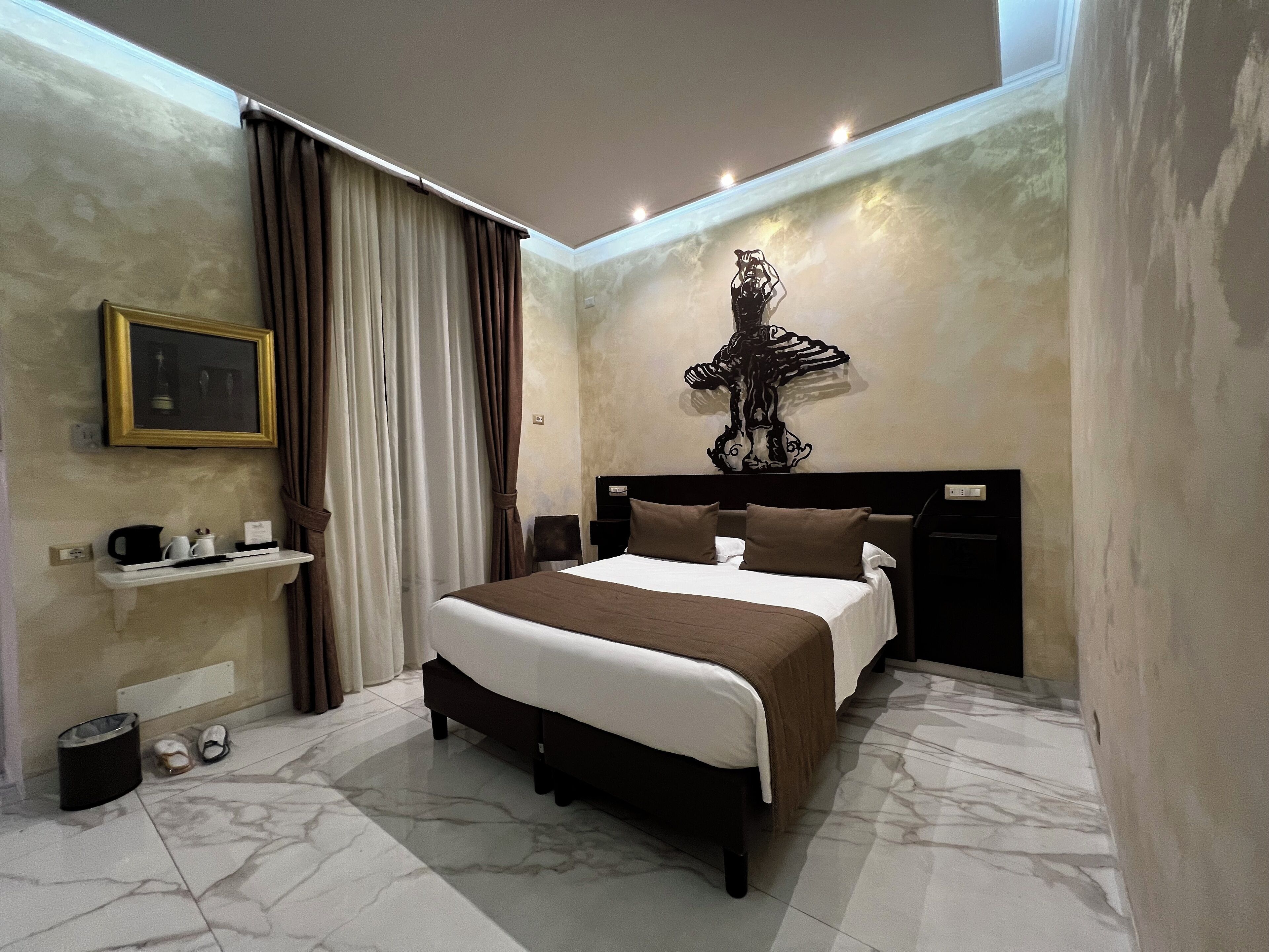 Une chambre à coucher moderne avec un grand lit, une tête de lit agrémentée d’un panneau décoratif, une table de chevet avec une lampe, un tableau encadré au mur et une fenêtre avec des rideaux.