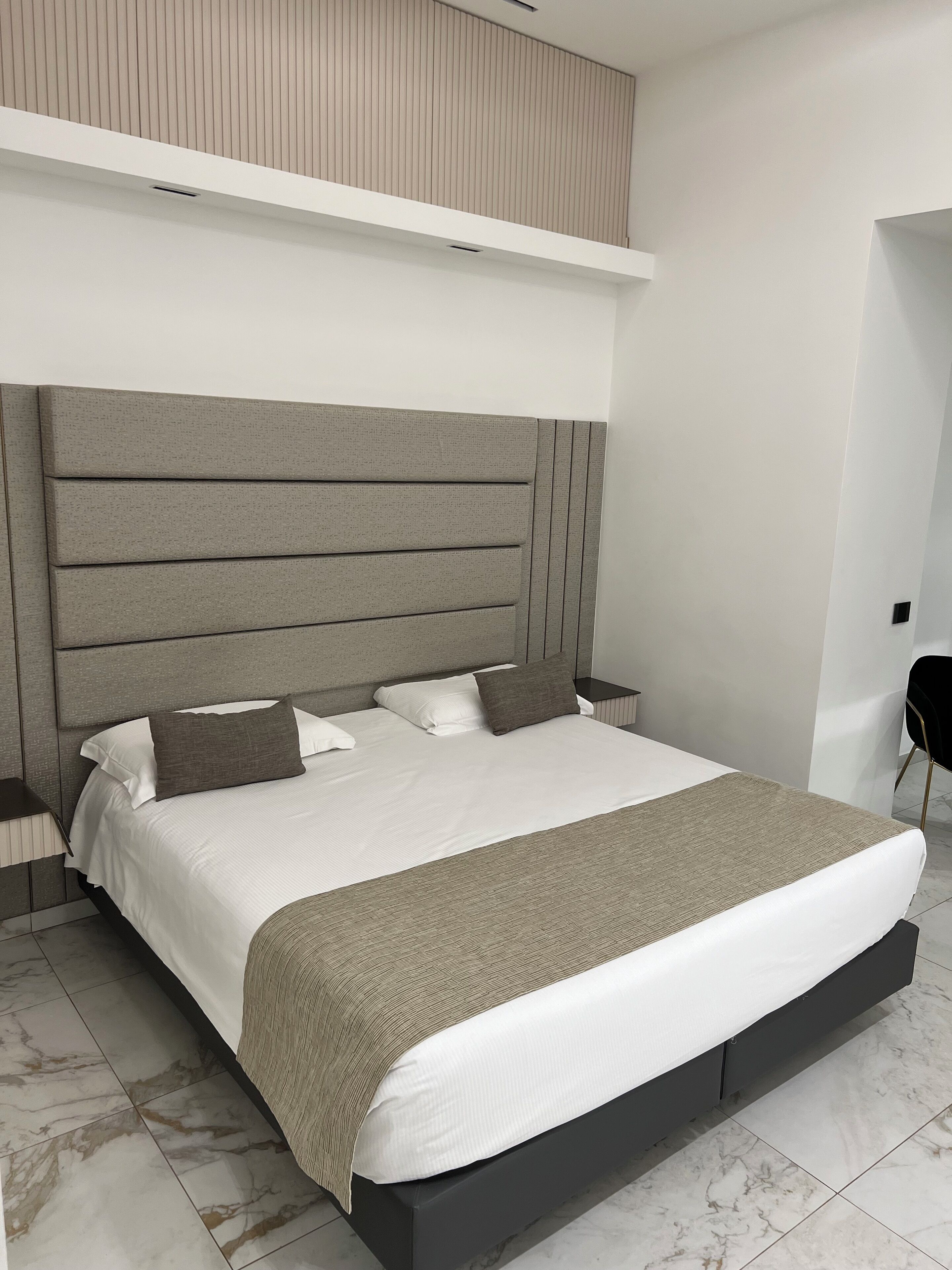 A modern bedroom with a large bed, a headboard with horizontal panels, a bedside table, and a chair.