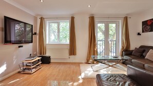 A modern living room with a leather sofa, a glass coffee table, and a mounted TV. - Austin David Apartments - Classic 2 Bed (London)