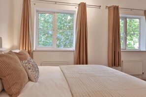 A bedroom with a bed, beige curtains, and a window with a view of trees.