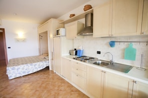 A compact kitchen with a bed, a microwave, a stove, and a sink.