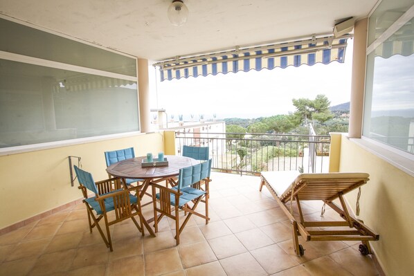 A balcony with a table and chairs, a wooden bench, and a view of the surrounding area.