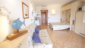 Una habitación compacta con sofá, dos camas, kitchenette y baño pequeño.