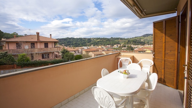 A balcony with a white table and chairs, overlooking a town with buildings and hills. - Appartamento La Caletta (Rio)