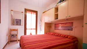 A bedroom with a large bed, a chair, a wardrobe, and a painting on the wall. - Appartamento La Caletta (Rio)