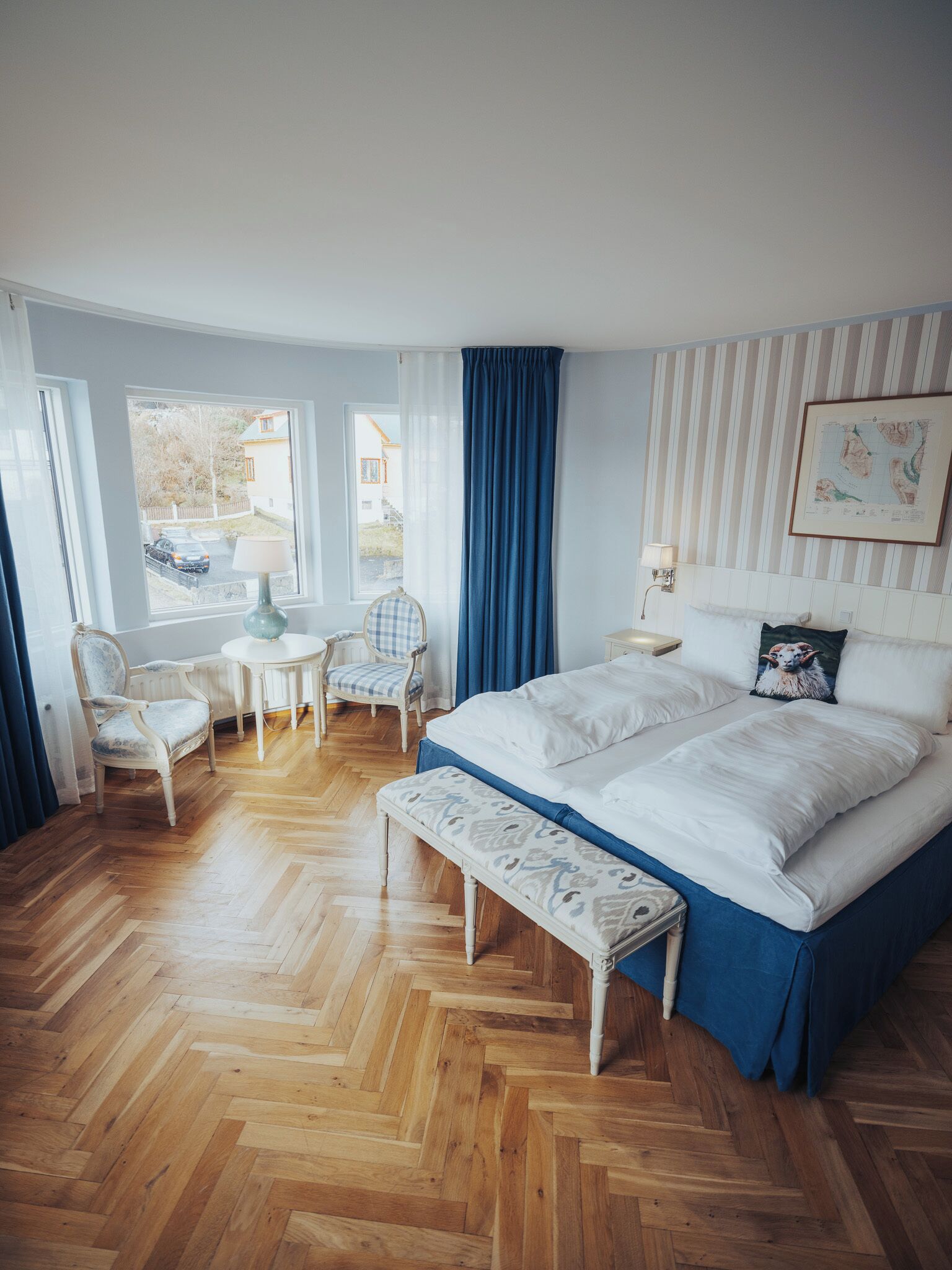 A bedroom with a large bed, a desk, two chairs, and a view of the outside.