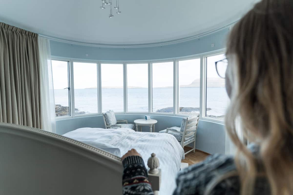 Ein Schlafzimmer mit großem Fenster zum Meer, einem Bett, einem kleinen Tisch und einem Stuhl.
