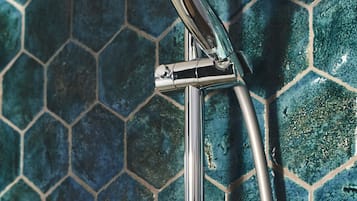 A showerhead with a modern design, mounted on a chrome fixture against a hexagonal tile wall.