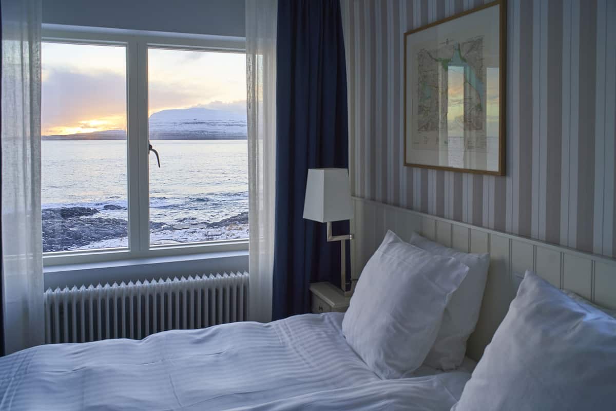 Ein Hotelzimmer mit Bett, Fenster mit Blick auf Meer und Berge, einer Lampe und einer Karte an der Wand.