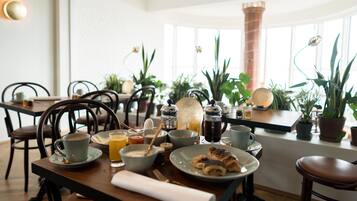 Une table mise pour le petit-déjeuner, avec une nappe, de l’assiette, des tasses et une cafetière, le tout préparé pour deux personnes.
