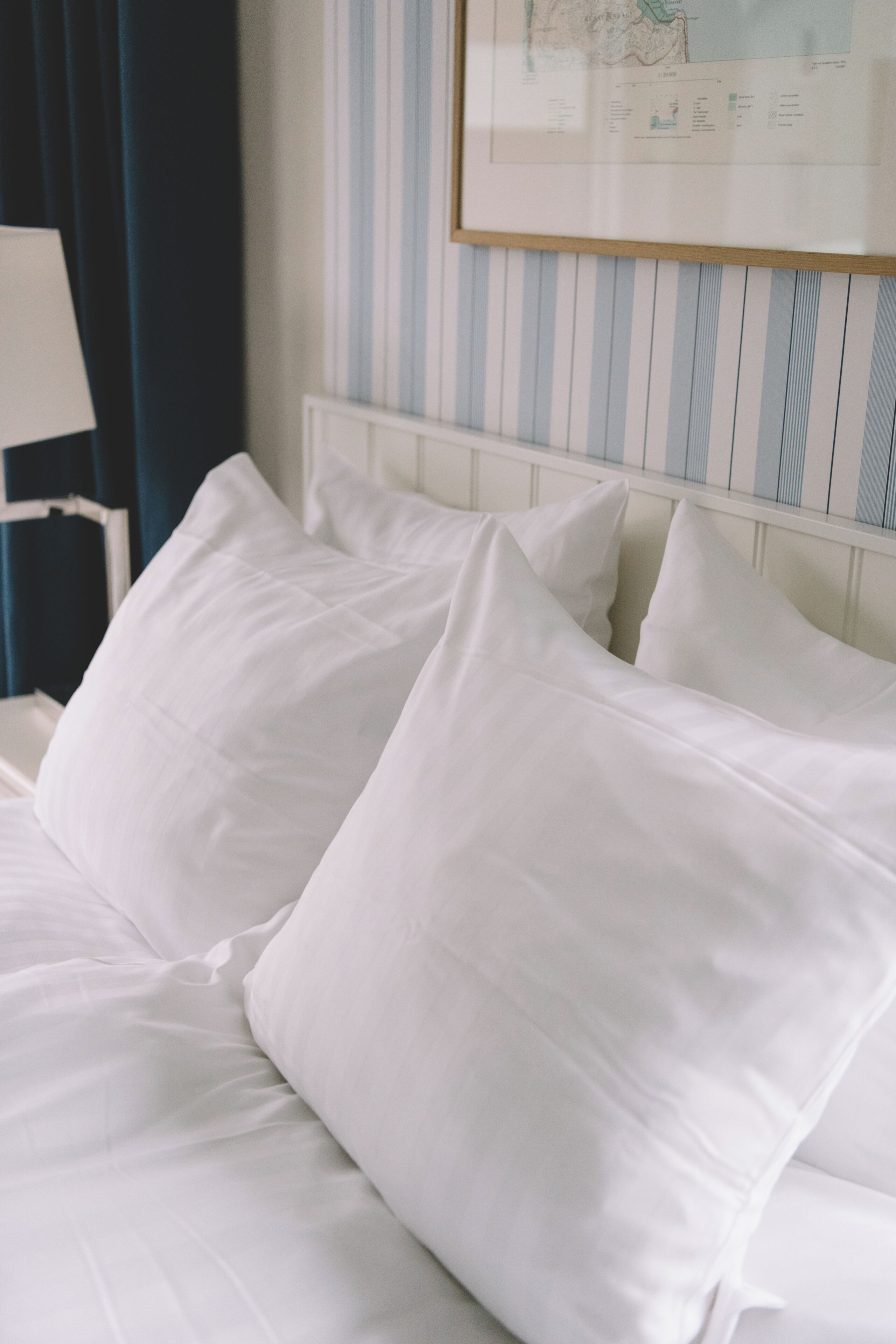 Un lit bien fait, avec du linge de lit blanc et des oreillers, un mur à rayures en arrière-plan et une carte encadrée accrochée au mur.