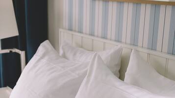Un lit bien fait, avec du linge de lit blanc et des oreillers, un mur à rayures en arrière-plan et une carte encadrée accrochée au mur.