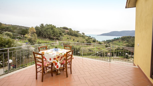 Eine Terrasse mit Esstisch, die auf eine reizvolle Landschaft mit Hügeln und einem Gewässer blickt.
