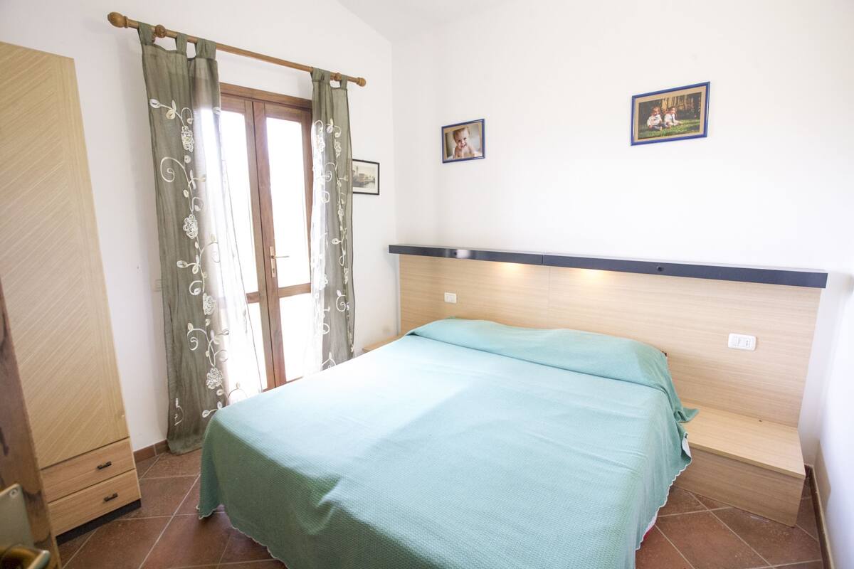 Ein Schlafzimmer mit einem Bett, einem Holzschrank, einer Tür mit Vorhang und zwei gerahmten Bildern an der Wand.