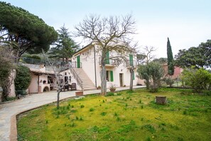 A traditional Mediterranean-style villa with a stone pathway leading to the entrance, surrounded by lush greenery and mature trees. - Appartamenti Lido di Capoliveri (Porto Azzurro)