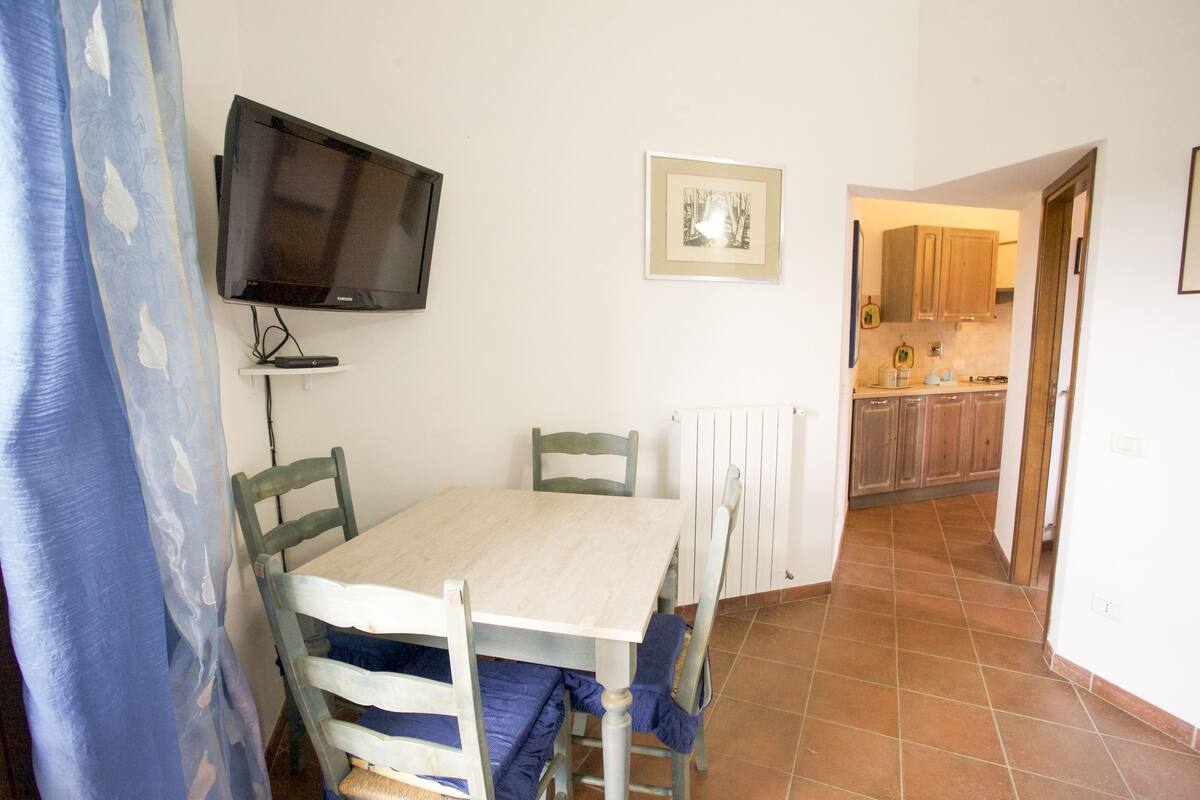 Ein Essbereich mit Tisch und Stühlen, einem an der Wand montierten Fernseher und einem gerahmten Bild.