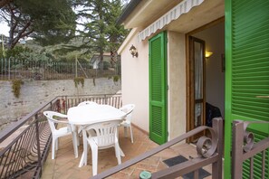 A balcony with a white table and chairs, green shutters, and a metal railing.