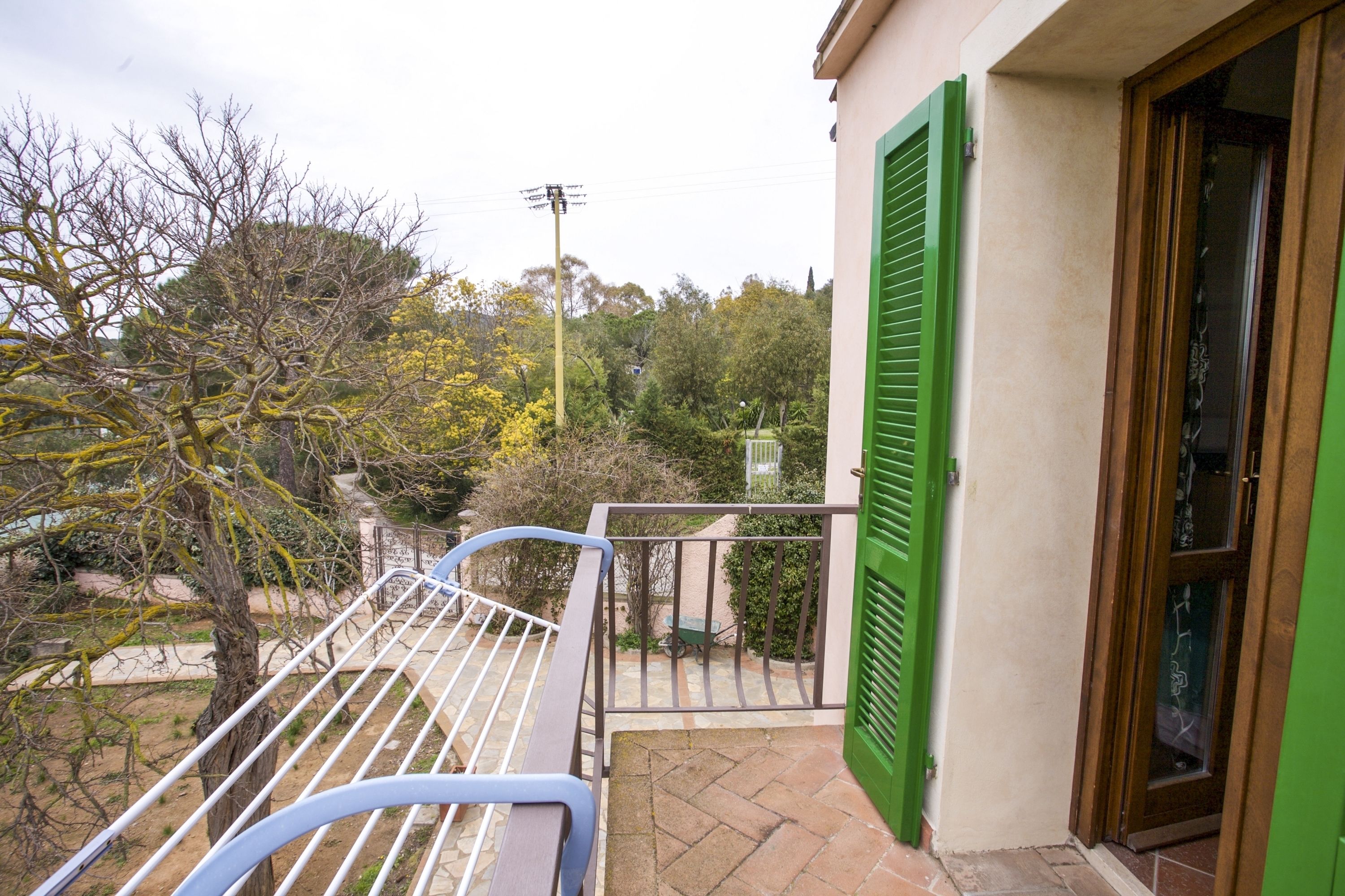 A balcony with a metal railing, a green shutter, and a door.