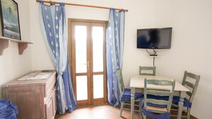Une pièce avec un bureau en bois, une chaise, un téléviseur fixé au mur et une porte ornée de rideaux bleus.