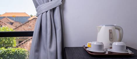 A window with a curtain tied back, a tray with two white cups and saucers, and a white kettle on a wooden table.