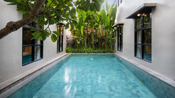 A rectangular swimming pool with clear blue water, surrounded by white walls and large windows. - The Aswana Seminyak (Seminyak)