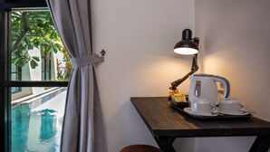 A room with a view of a swimming pool, a table with a kettle, cups, and a tray, and a wooden stool. - The Aswana Seminyak (Seminyak)