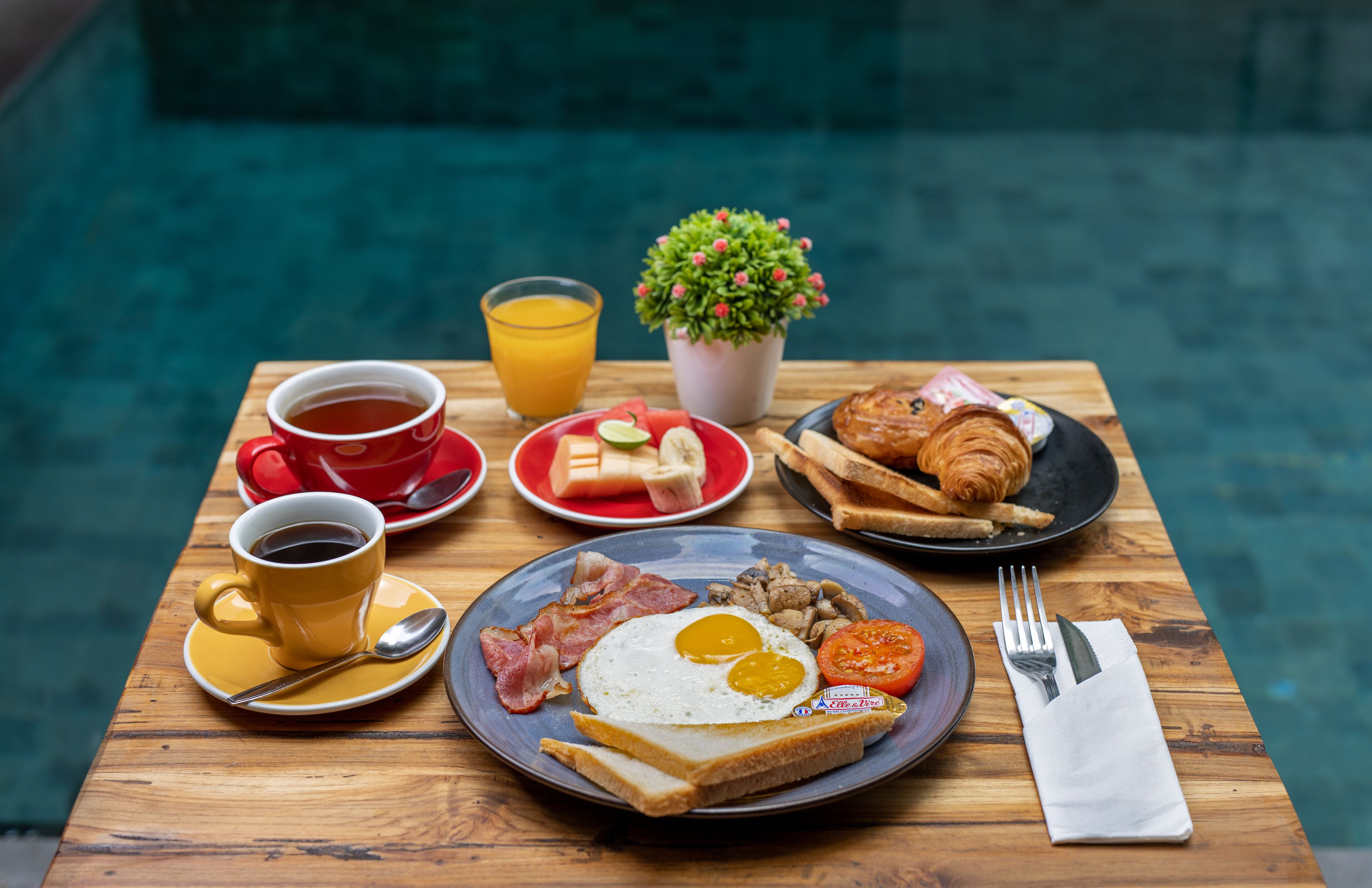 A breakfast table with toast, eggs, bacon, tomatoes, and a croissant.
