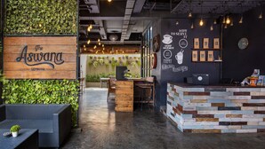 A cozy cafe interior with a wooden sign reading "The Aswara Seminyak," a counter with a coffee machine, and a wall decorated with coffee-related illustrations and a clock. - The Aswana Seminyak (Seminyak)