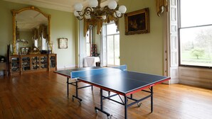 A room with a ping pong table, wooden flooring, a chandelier, a large mirror, and a window with a view. - Temple House (Kilvarnet)