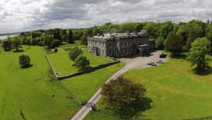A large, historic building with a symmetrical facade, surrounded by lush green fields and trees. - Temple House (Kilvarnet)