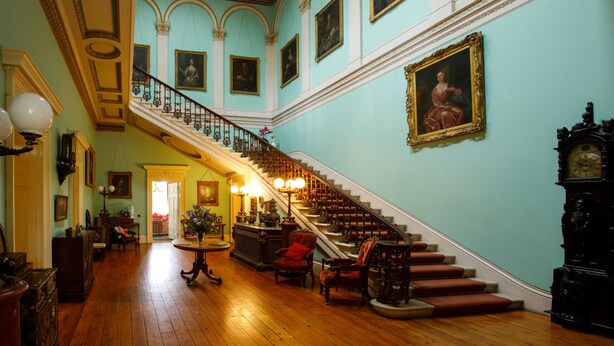 A grand staircase with ornate railings and a chandelier, leading to a room with classical architecture and framed artwork on the walls. - Temple House (Kilvarnet)