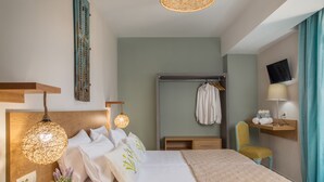 A hotel room with a bed, bedside lamp, a wall-mounted TV, a wooden headboard, a hanging light fixture, a towel rack, and a small shelf with towels. - Bruma Luxury Residence (Zakynthos)