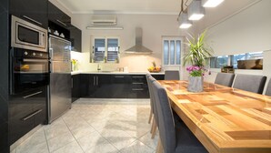 A modern kitchen with dark cabinetry, stainless steel appliances, and a wooden dining table with chairs. - Bruma Luxury Residence (Zakynthos)