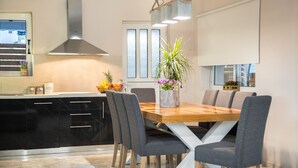 A modern kitchen with a wooden dining table, grey chairs, and a central island with a plant. - Bruma Luxury Residence (Zakynthos)