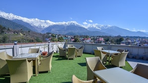 Een terras op het dak met rieten meubilair en kunstgras, met uitzicht op een stad en besneeuwde bergen.