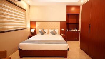 A hotel room with a large bed, a bedside table with a lamp, a wardrobe, and a small desk with a chair.