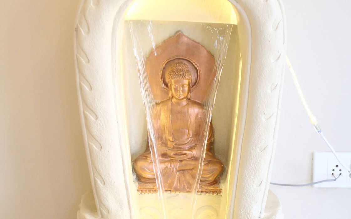 A statue of a seated figure with water flowing from its head, encased in a white, textured container.